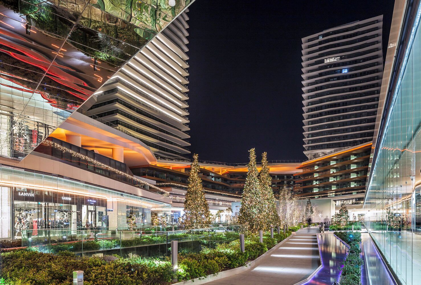 A modern urban shopping area with glass railings, a central walkway, and adjacent high-rise buildings.