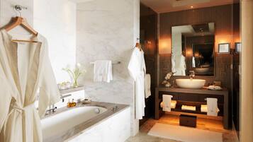 A modern bathroom with a marble bathtub, a large vanity with a sink, and a mirror above the vanity.