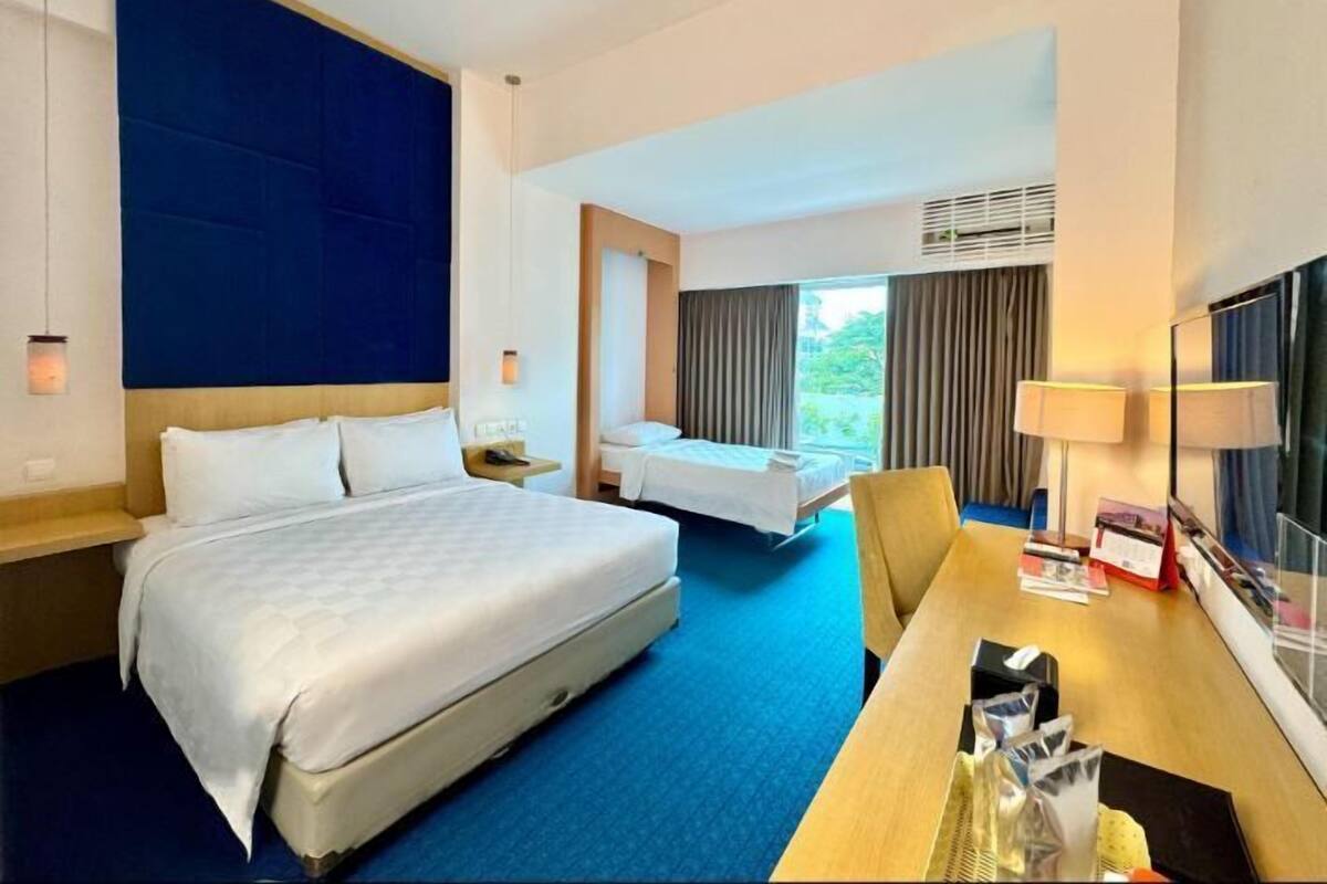 Une chambre d’hôtel avec un grand lit, un lit plus petit, un bureau et une télévision.