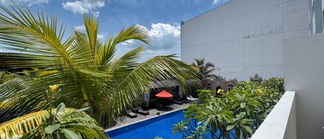 Una piscina en la azotea con palmeras y un edificio blanco al fondo.