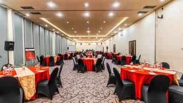 Un salón de conferencias con varias mesas, sillas negras y manteles rojos.