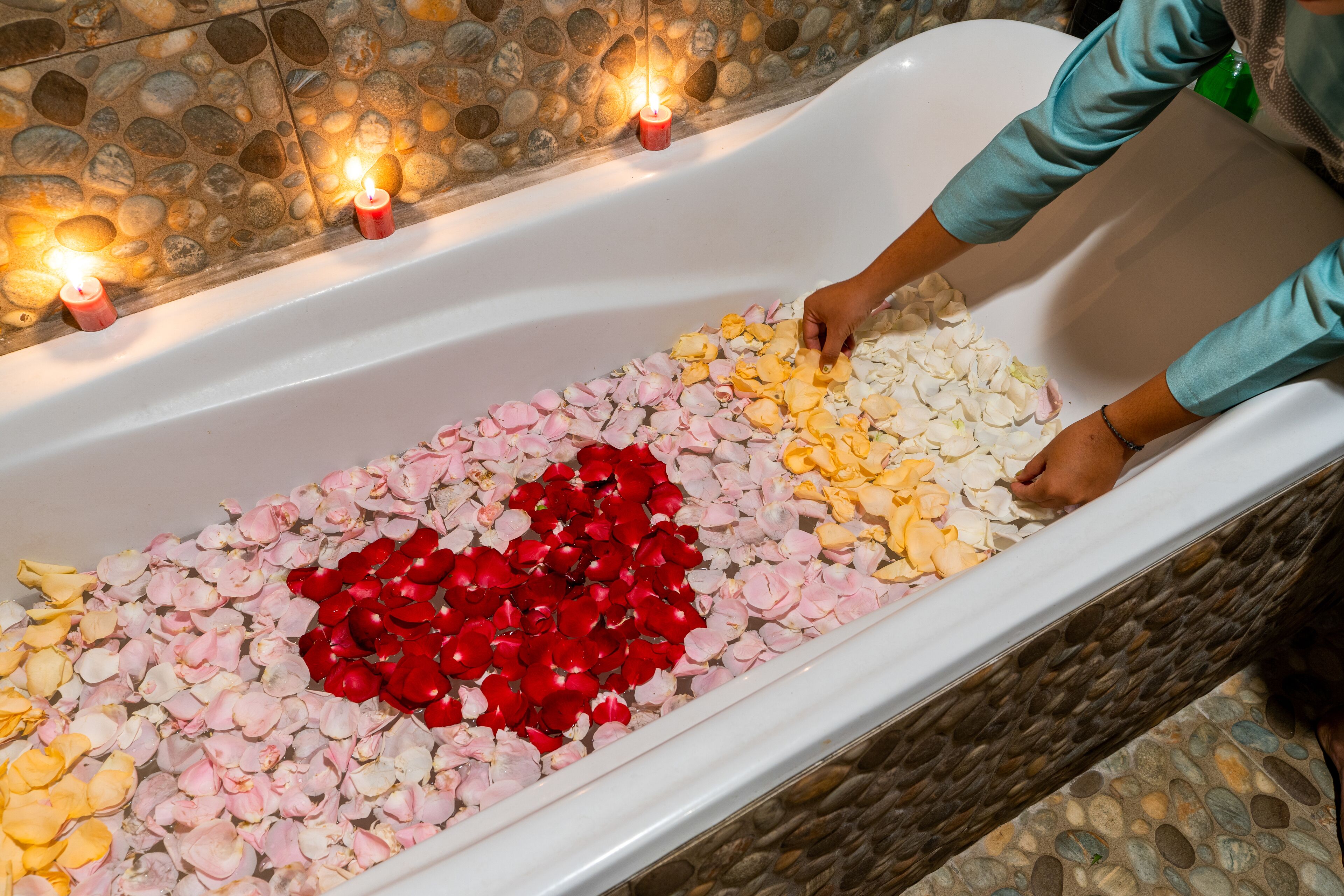 A bathtub filled with rose petals in various colors, with candles placed along the edge.