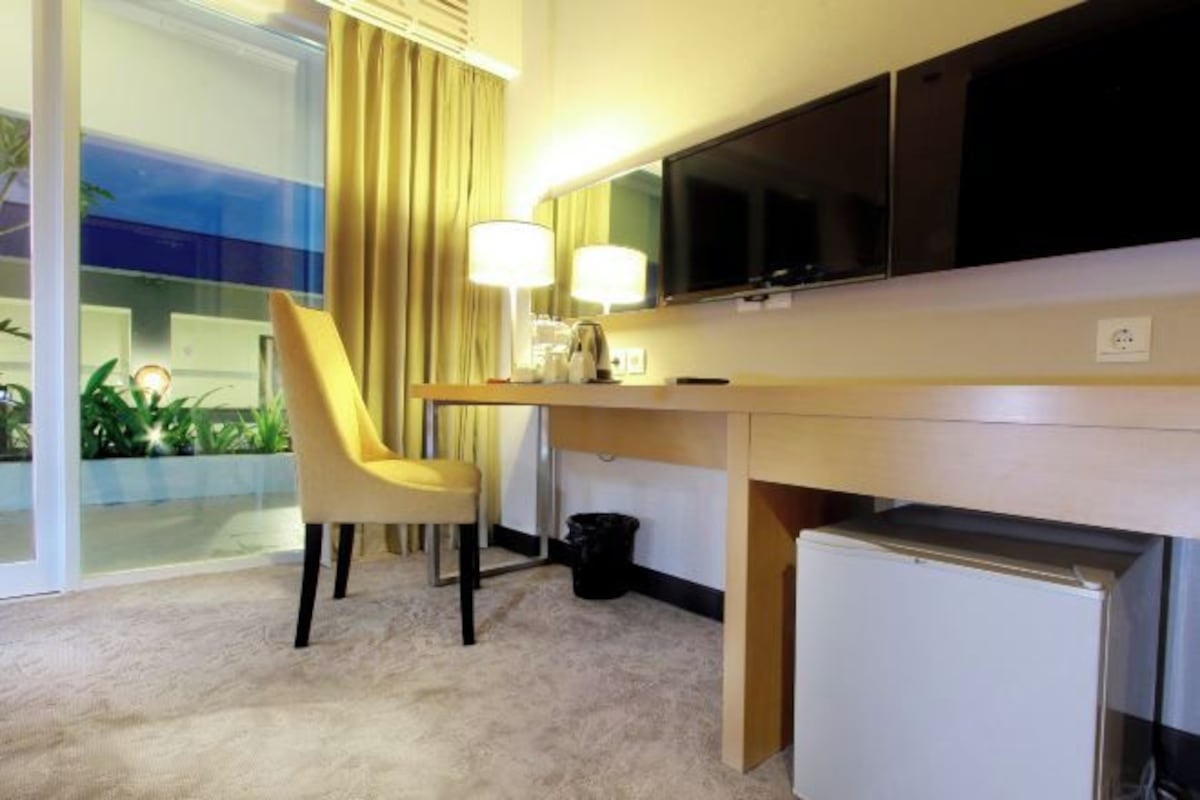 Habitación de hotel con escritorio, silla, televisión y un refrigerador pequeño.