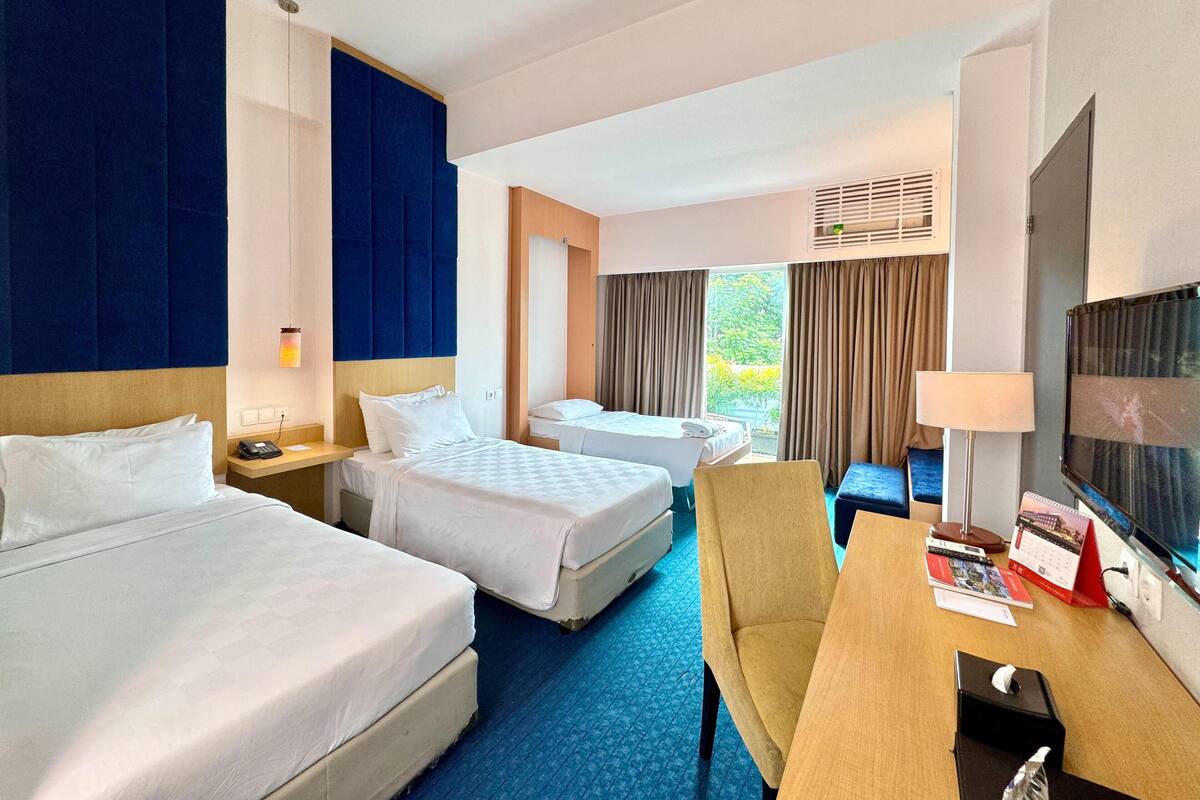 Une chambre d’hôtel avec deux lits, un bureau, une chaise, une télévision et une fenêtre avec des rideaux.