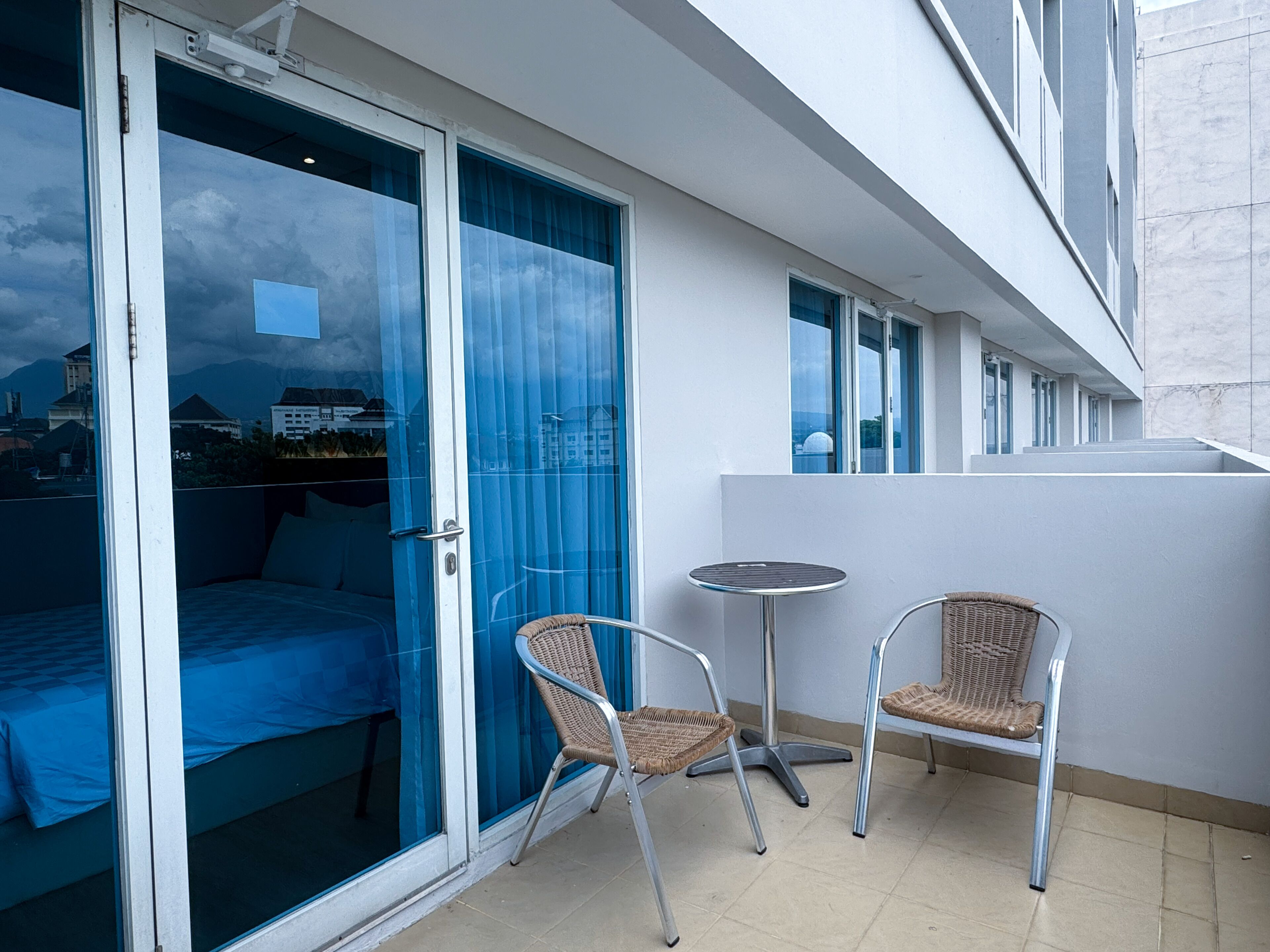 A balcony with a bed, two wicker chairs, and a small round table.