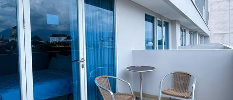 A balcony with a bed, two wicker chairs, and a small round table.