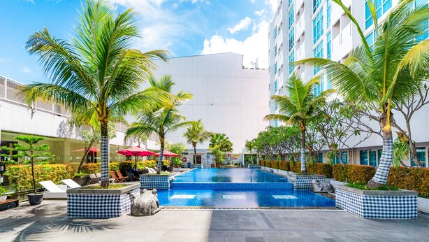 A swimming pool with lounge chairs and palm trees, surrounded by a modern building with large windows. - Swiss-Belinn Malang (Malang)