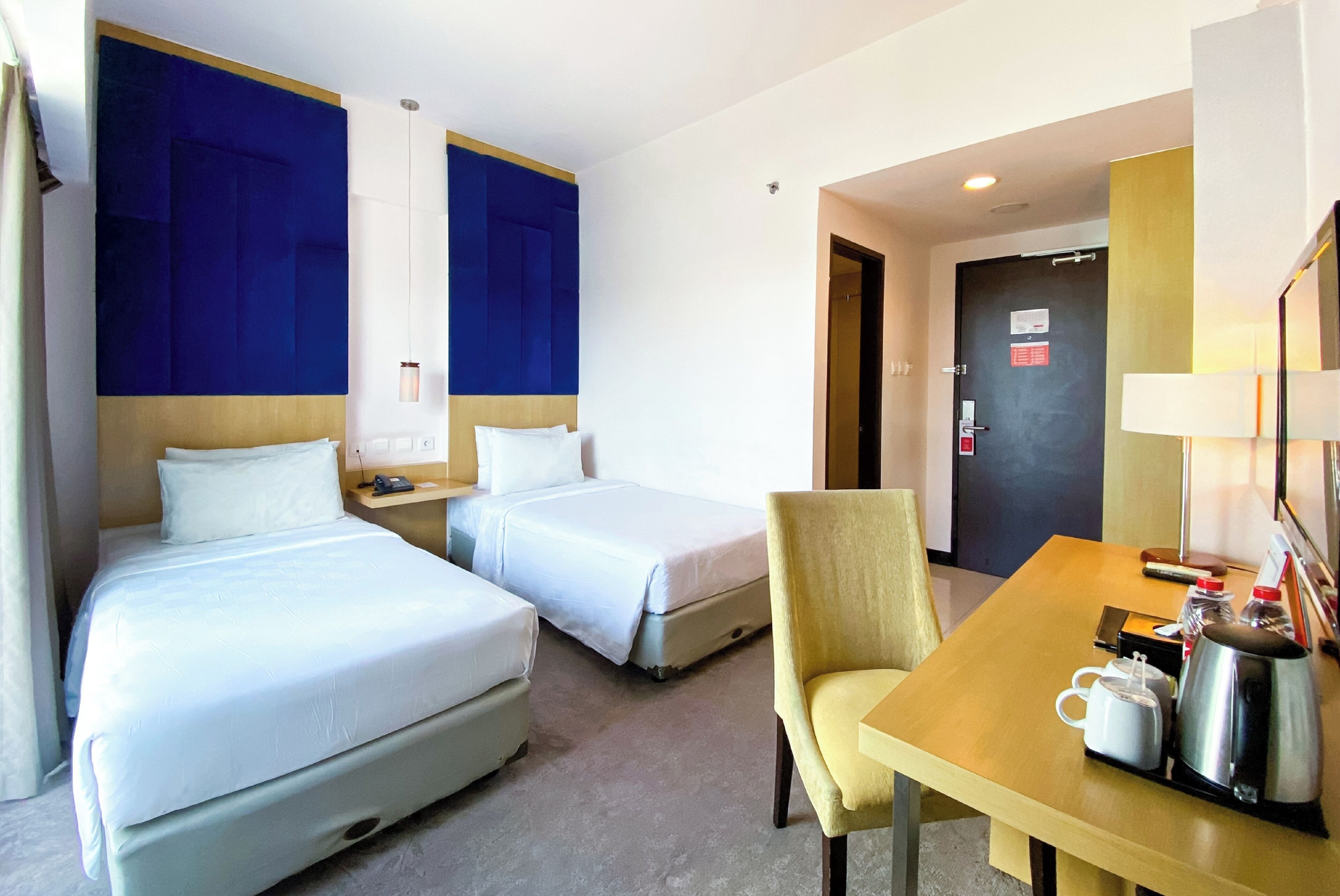 A hotel room with two beds, a desk with a chair, a coffee maker, and a door with a sign.