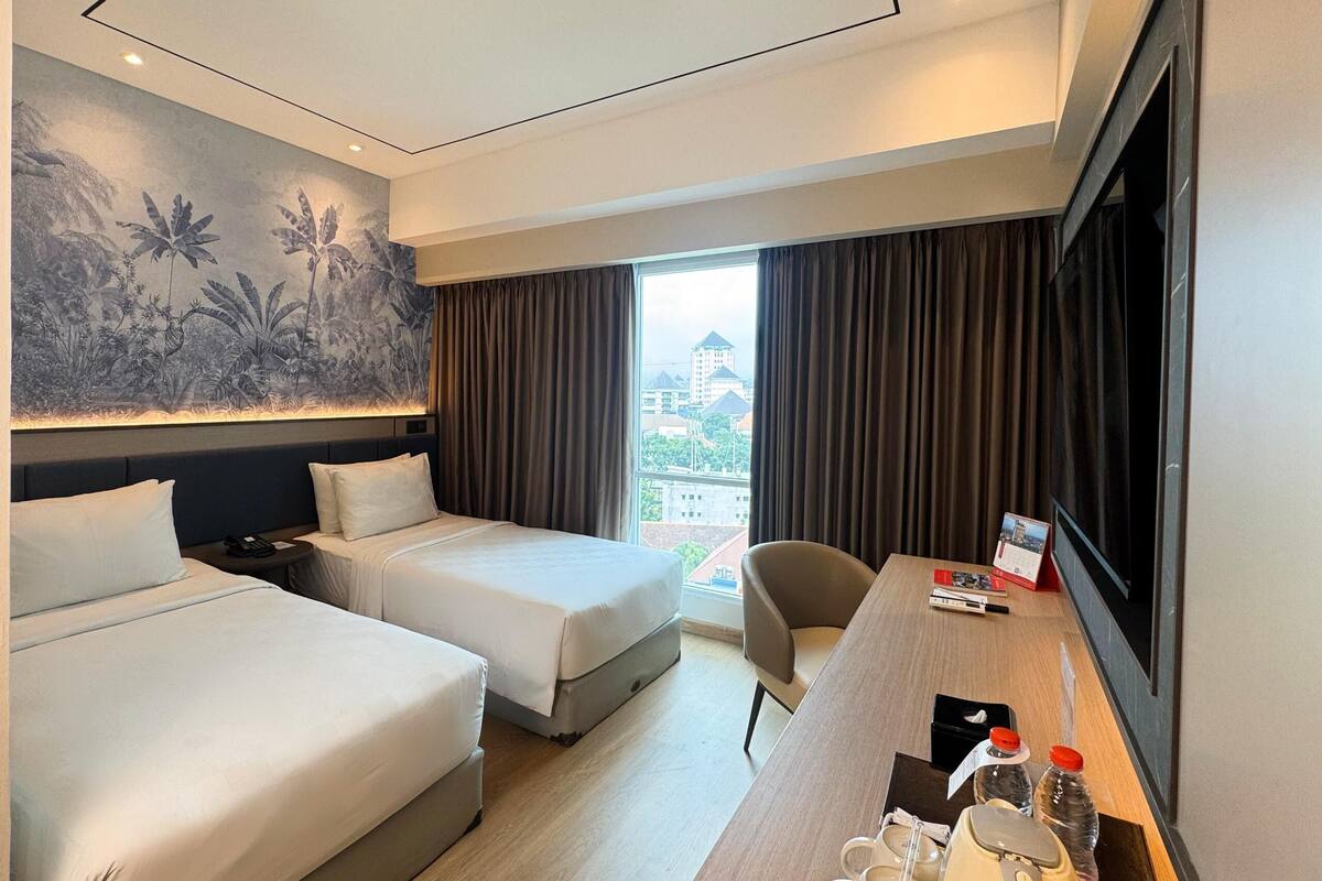 Une chambre d’hôtel avec deux lits, un bureau avec une télévision, une fenêtre avec des rideaux et un mur orné d’une fresque sur le thème de la nature.