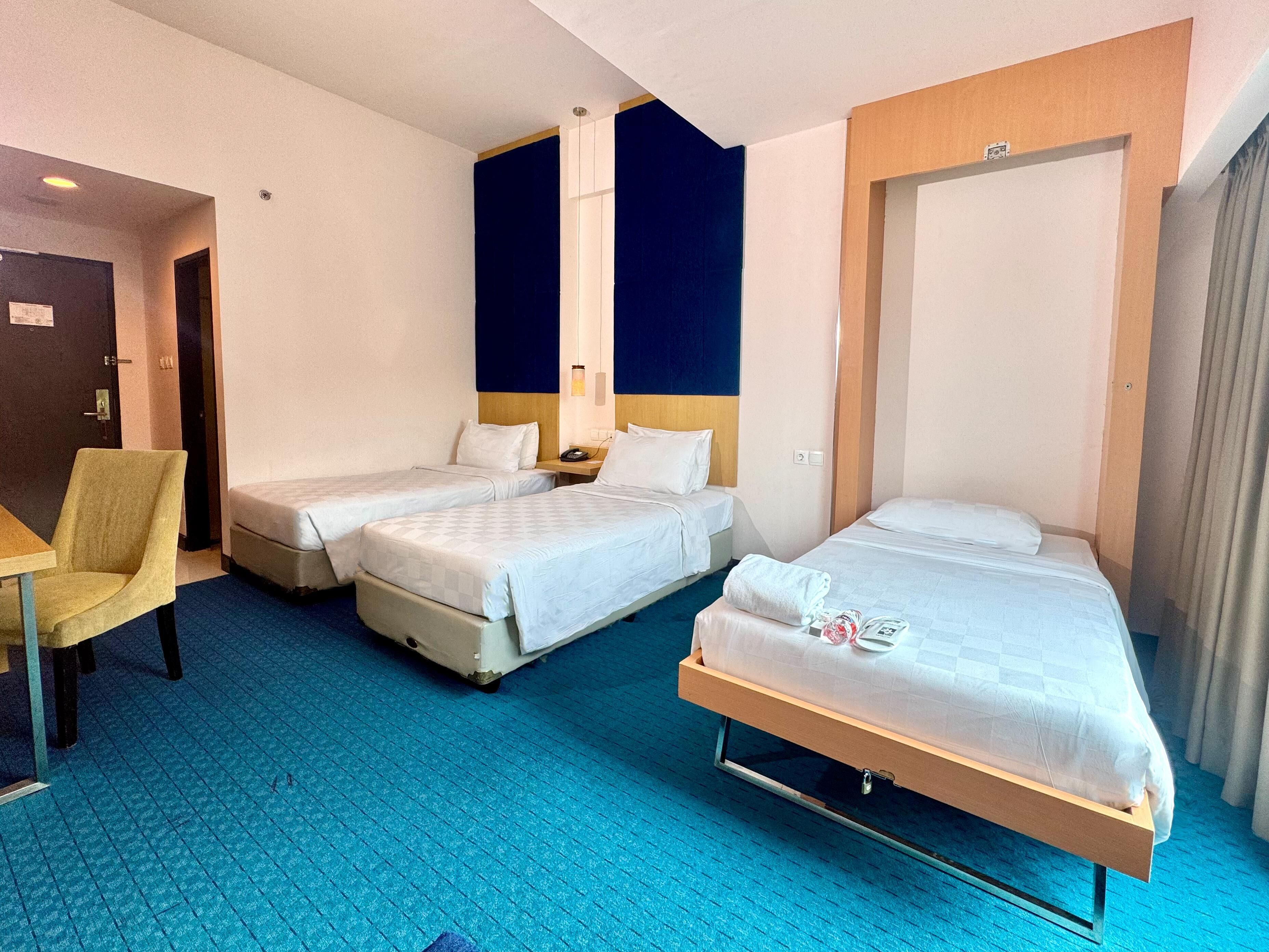 A hotel room with two single beds, a desk with a chair, and a large window.