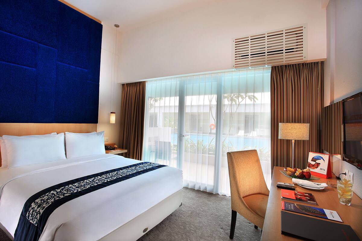 Une chambre d’hôtel avec un grand lit, un bureau avec une chaise, une télévision et une fenêtre avec des rideaux.