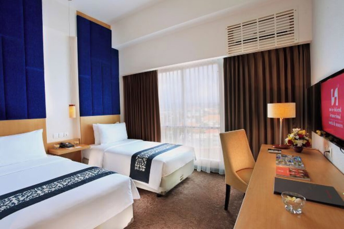 Habitación de hotel con dos camas, un escritorio, una silla, un televisor y una ventana con cortinas.
