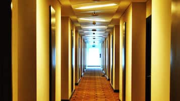 Corridoio d'hotel con tappeto a motivi, porte su entrambi i lati e una ventola a soffitto.
