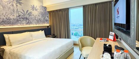 A hotel room with a bed, a desk with a chair, a television, and a view of the city through large windows.