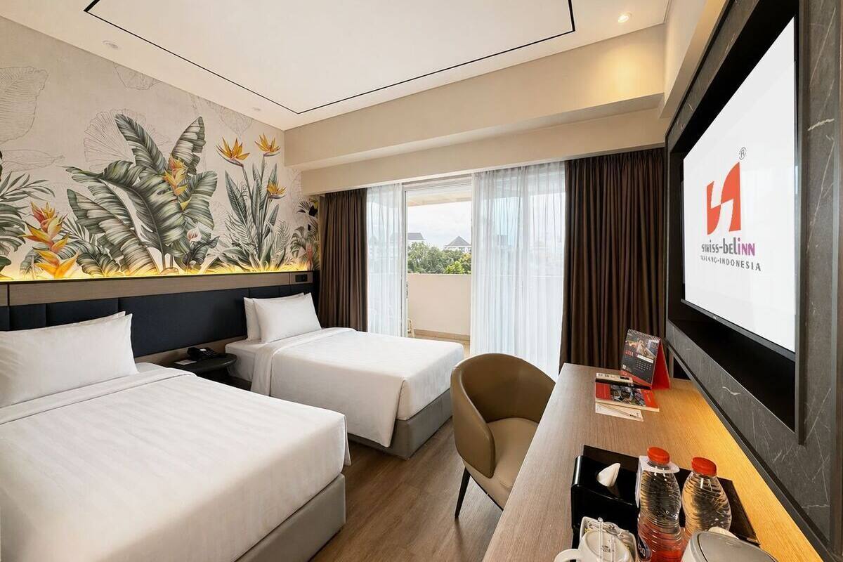 Une chambre d’hôtel avec deux lits, un bureau avec un ordinateur, une télévision et une fresque murale.