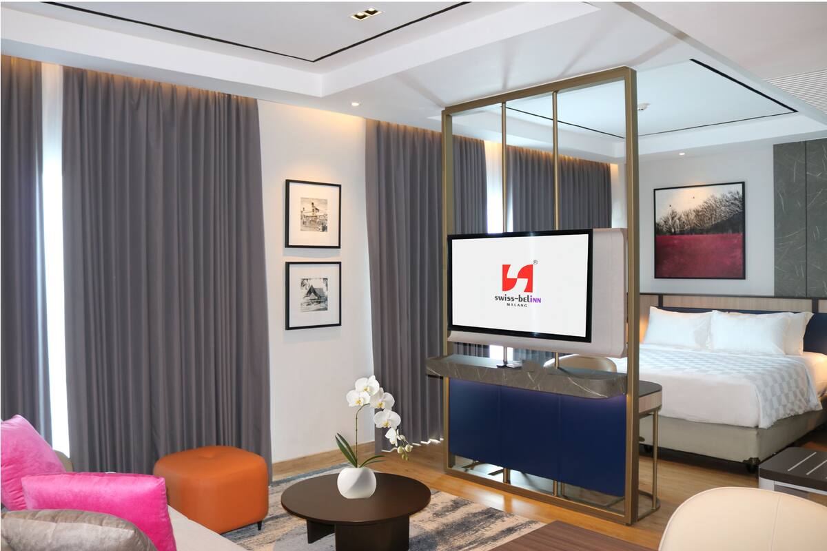 Une chambre d’hôtel moderne équipée d’un lit, d’un bureau, d’une télévision et d’une grande fenêtre avec des rideaux.