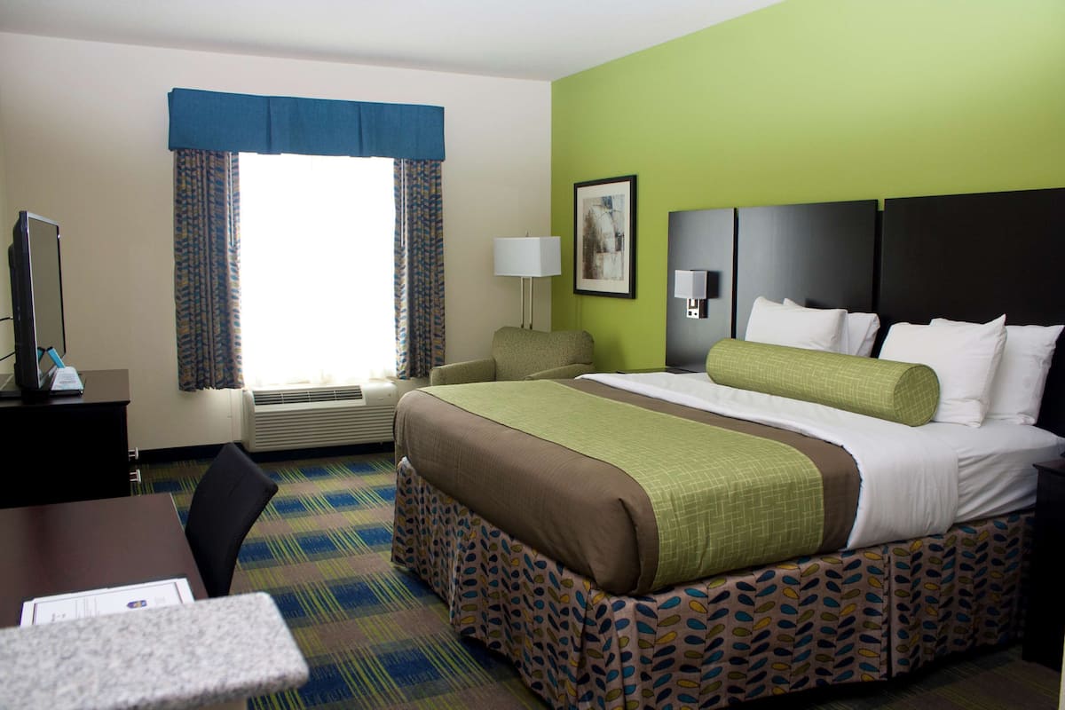Habitación de hotel con cama, escritorio, silla, lámpara y ventana con cortinas.
