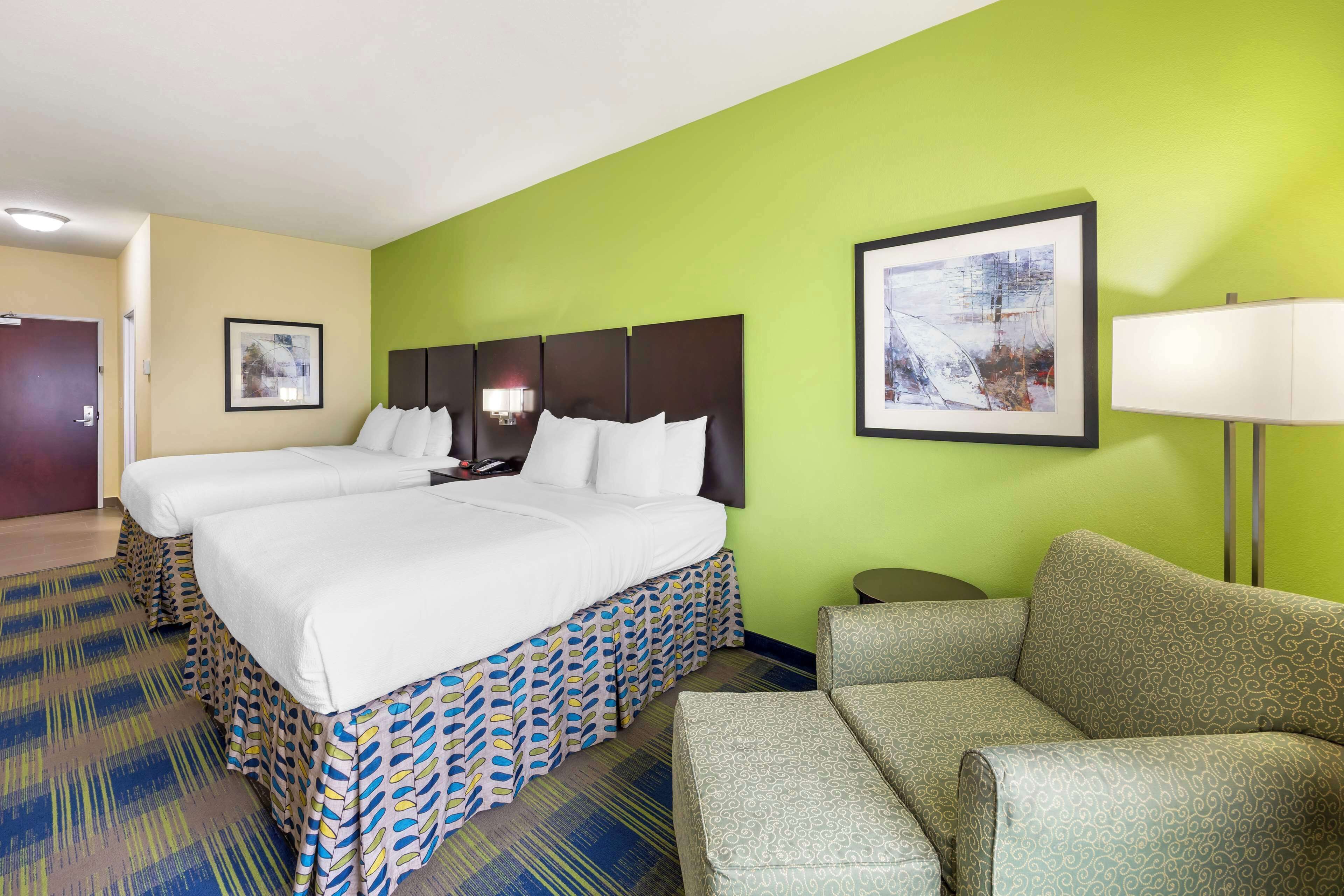 A hotel room with two beds, a green wall, a framed picture, a lamp, and a patterned carpet.