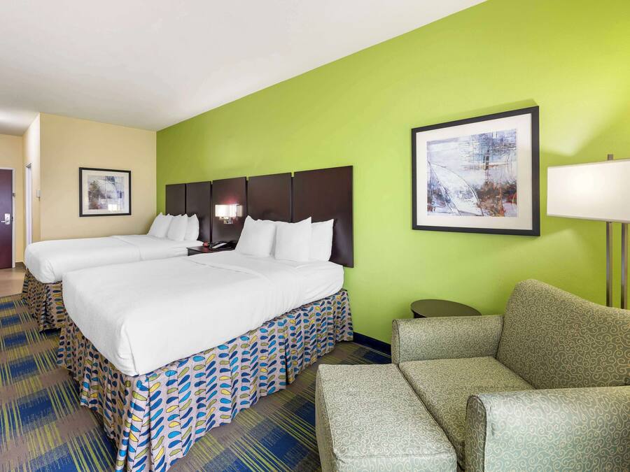 A hotel room with two beds, a green wall, a framed picture, a lamp, and a patterned carpet.