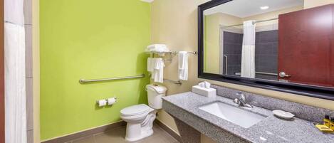 A bathroom with a green wall, a white toilet, a sink with a mirror, and a shower area.