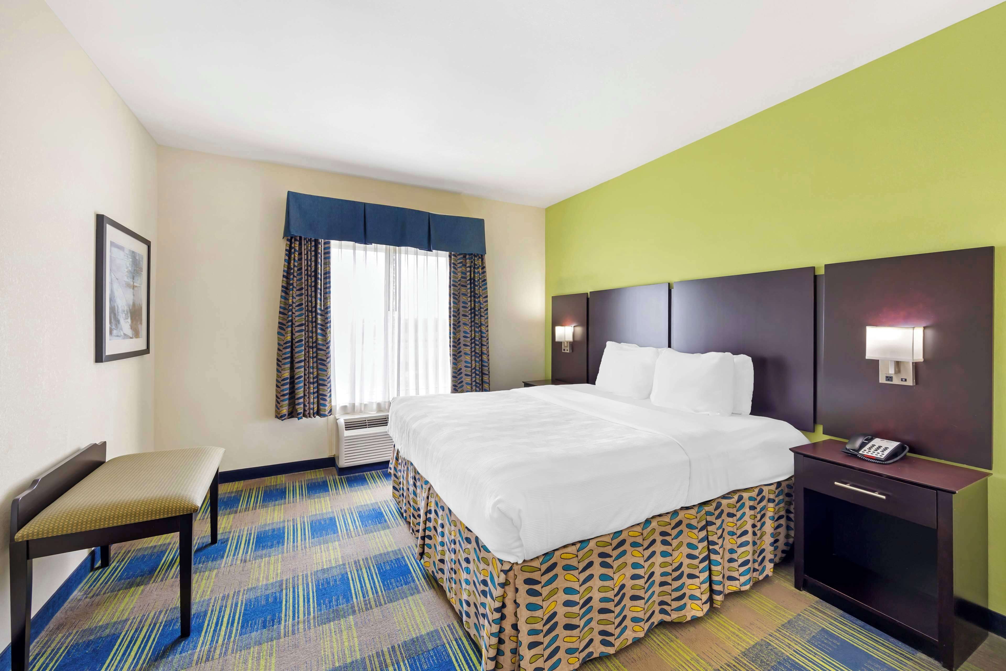 A hotel room with a bed, bedside table, chair, and a window with curtains.