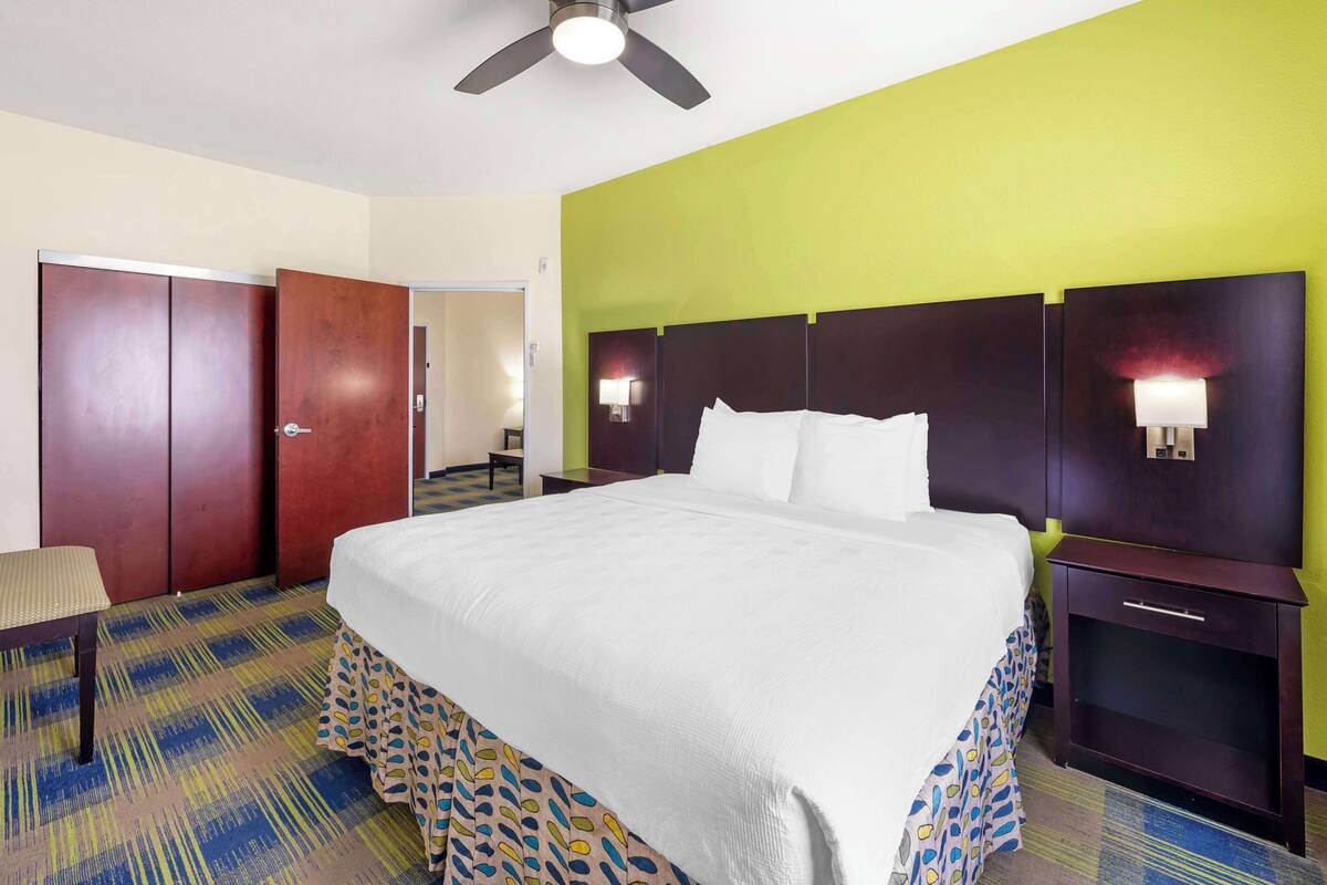 Una habitación de hotel con cama, mesita de noche, silla, armario y ventilador de techo.