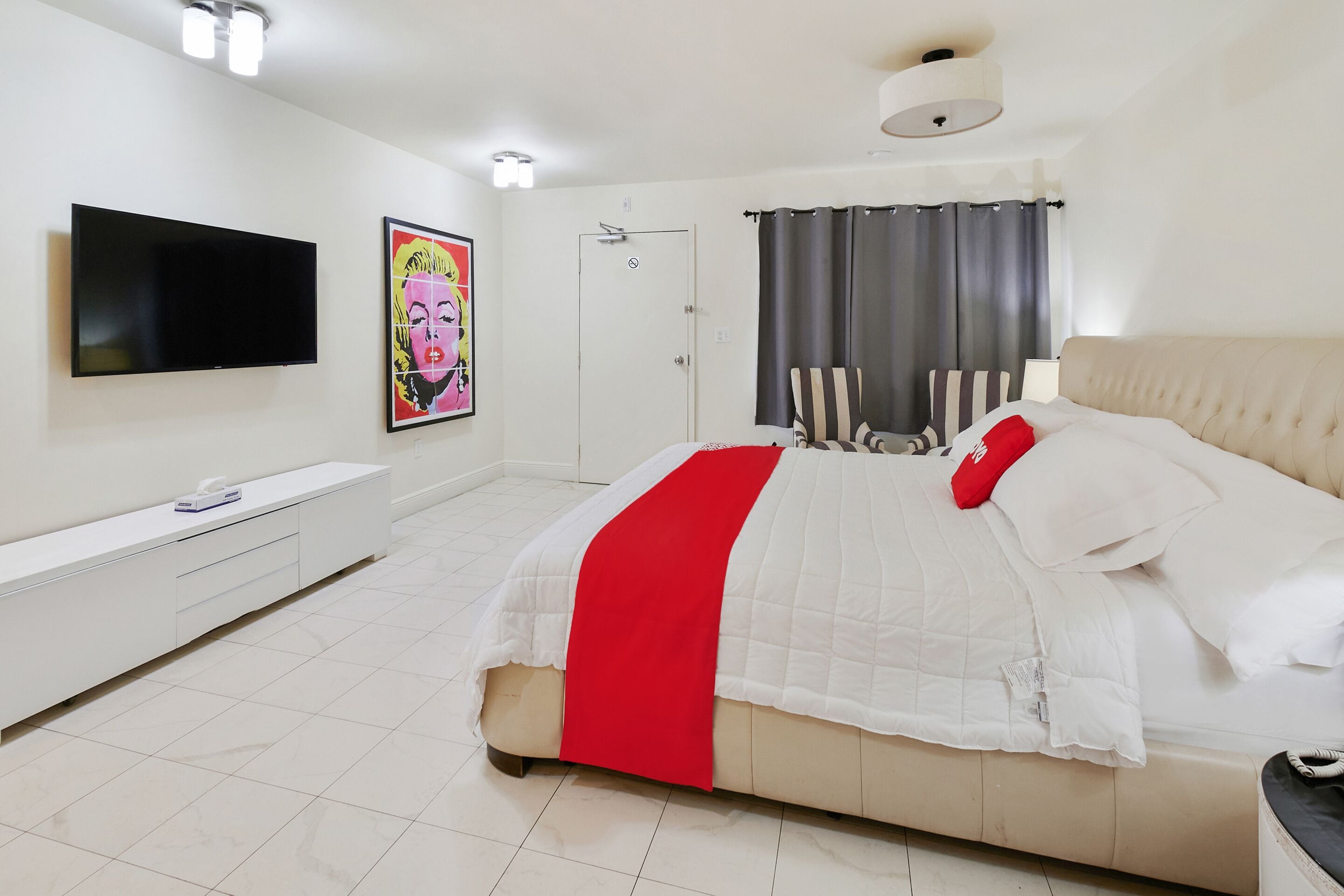 Een moderne slaapkamer met een bed, een televisie, een nachtkastje en een deur.