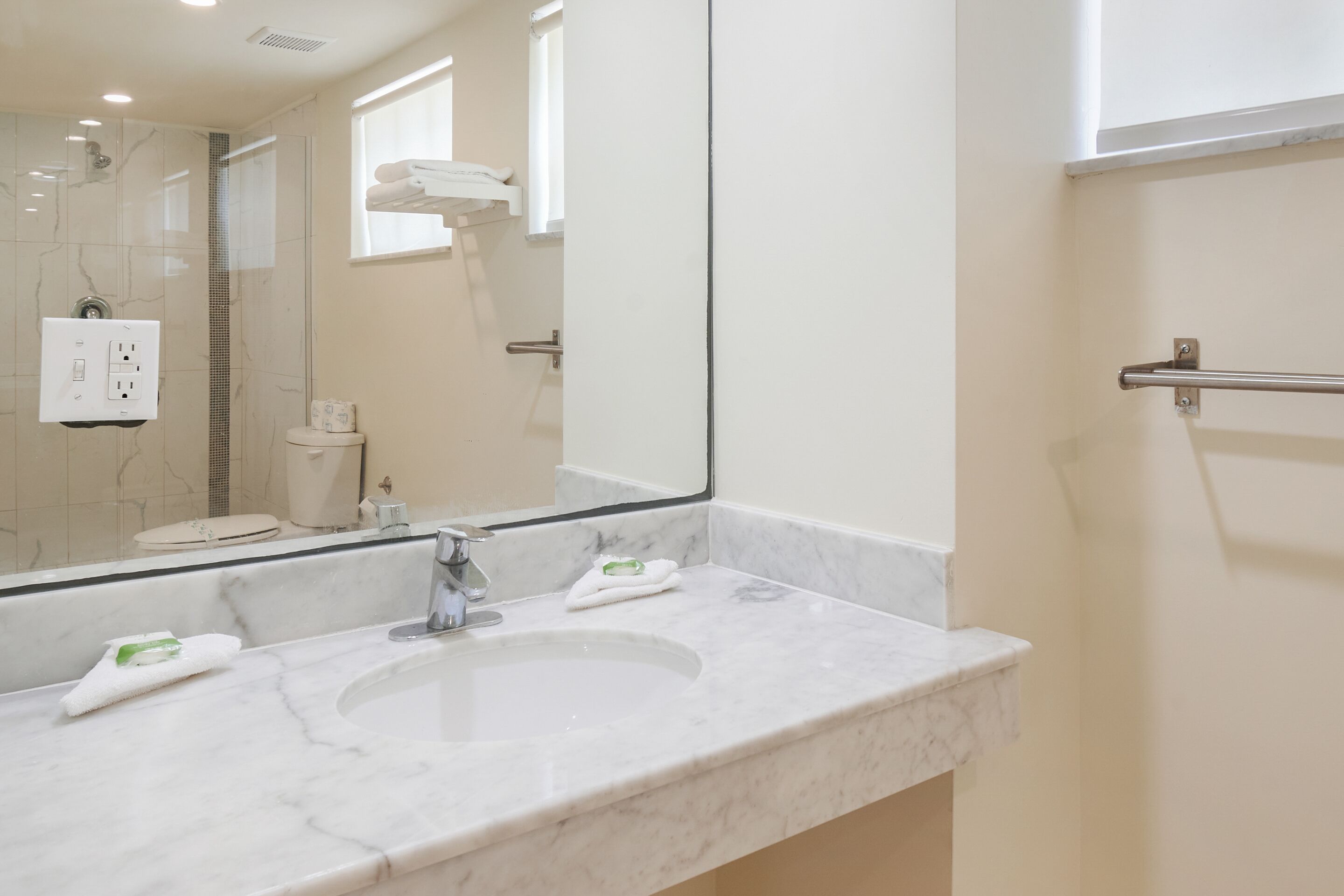 Un baño con lavamanos de mármol blanco, un espejo grande y un perchero para toallas.