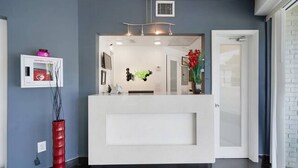 A reception area with a white counter, a red vase, and a wall-mounted device. - Gables Cove Hotel (Coral Gables)