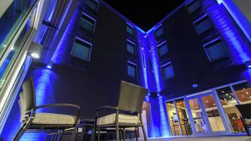 Un edificio con varios pisos y una zona de estar al nivel de la calle con sillas.