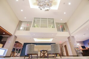 A hotel lobby with a high ceiling, a chandelier, a seating area with two chairs, a reception desk, and a staircase leading to an upper level. - Holiday Inn Express & Suites Miami Airport East by IHG (Miami)