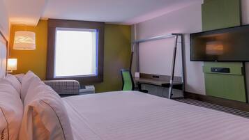 A hotel room with a bed, a desk, a chair, a television, and a window.