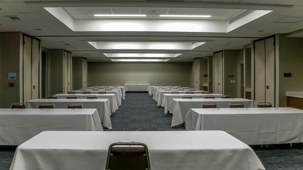 Une salle de conférence avec des rangées de tables et de chaises, équipée de plaques nominatives et de stylos, et un panneau indiquant la sortie sur le mur.