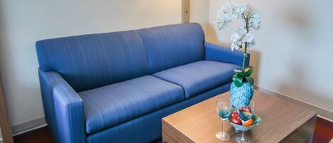 A room with a blue sofa, a wooden coffee table with a vase of flowers, and a lamp on the wall.