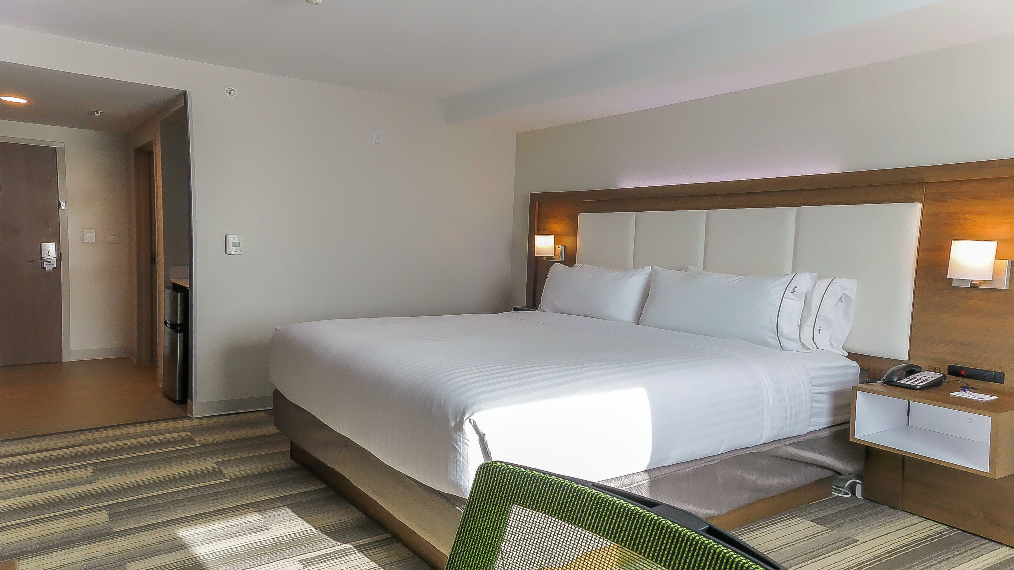 A hotel room with a large bed, a bedside table with a phone, and a door leading to a hallway.