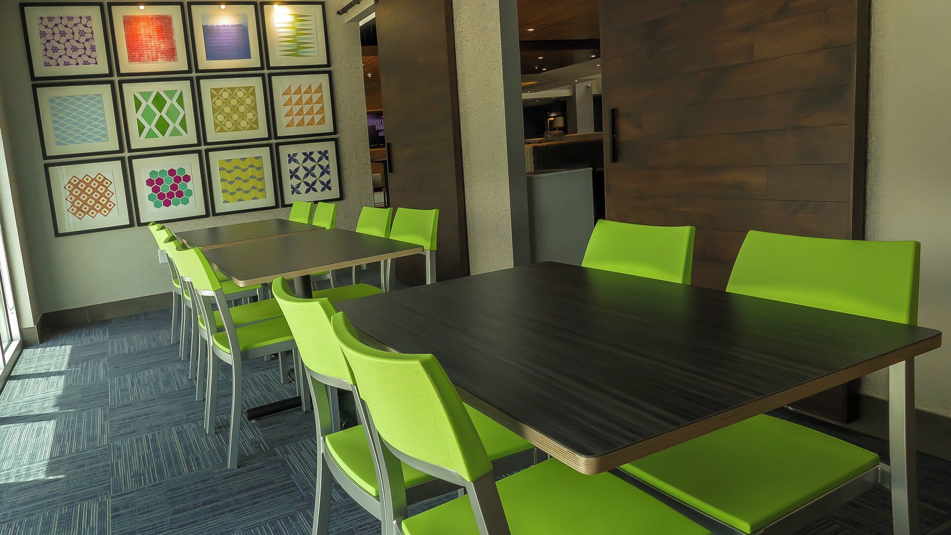 Une salle de conférence avec une table rectangulaire et six chaises vertes, un mur à motifs et un sol recouvert de moquette.