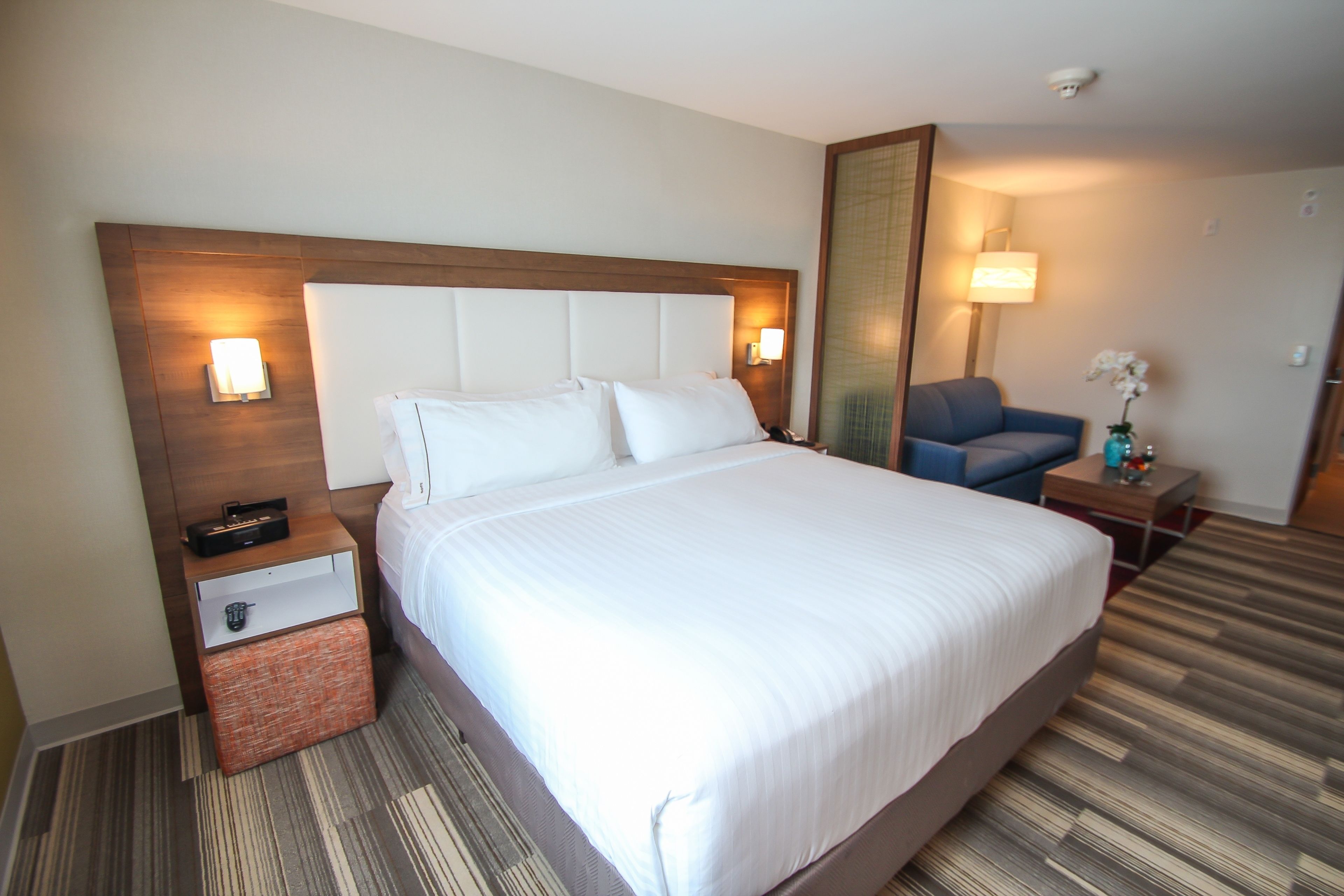 A hotel room with a large bed, a nightstand, a chair, and a mirror.