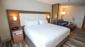 A hotel room with a large bed, a nightstand, a chair, and a mirror.