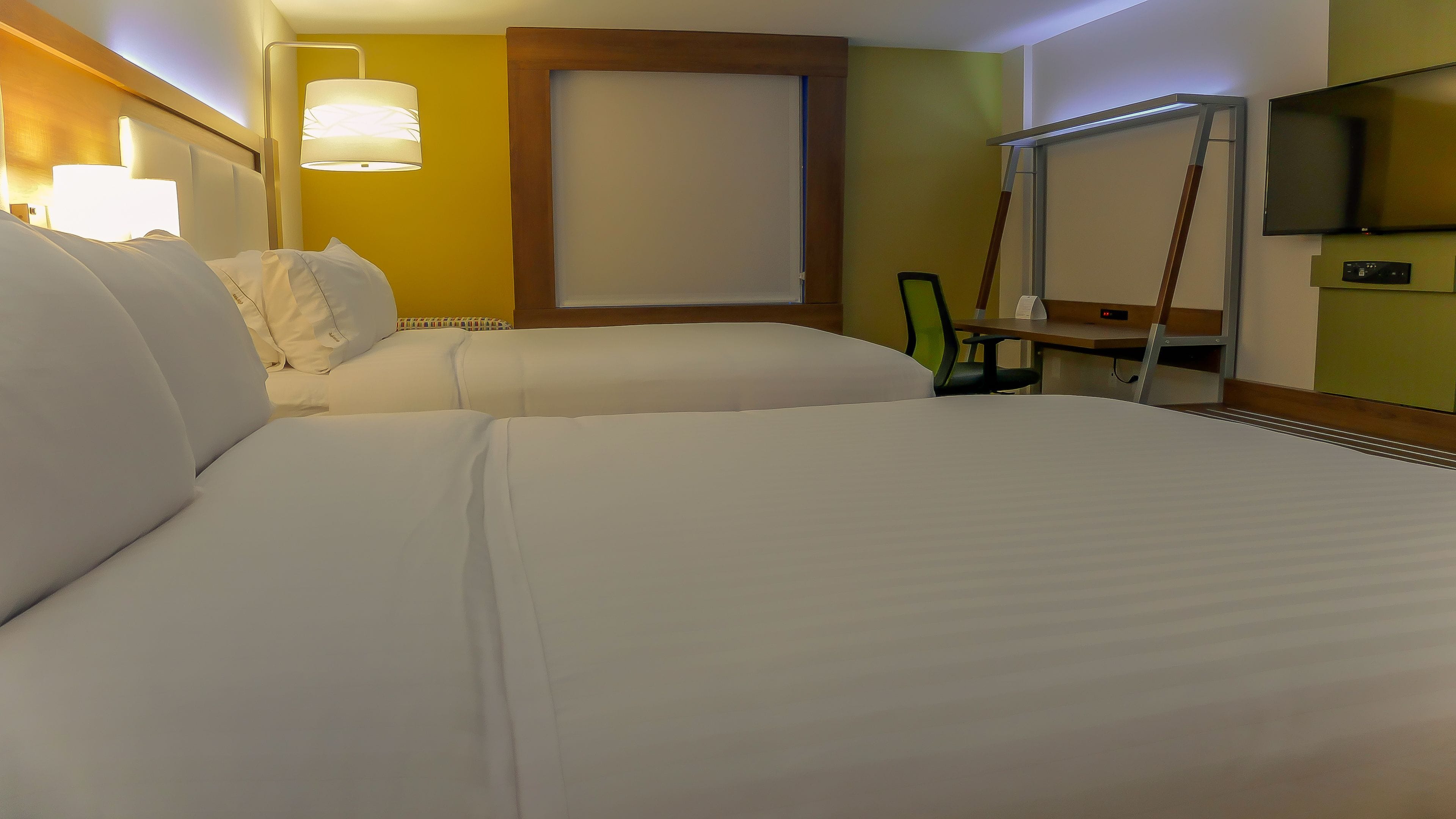 A hotel room with two beds, a desk, a chair, a TV, and a window.