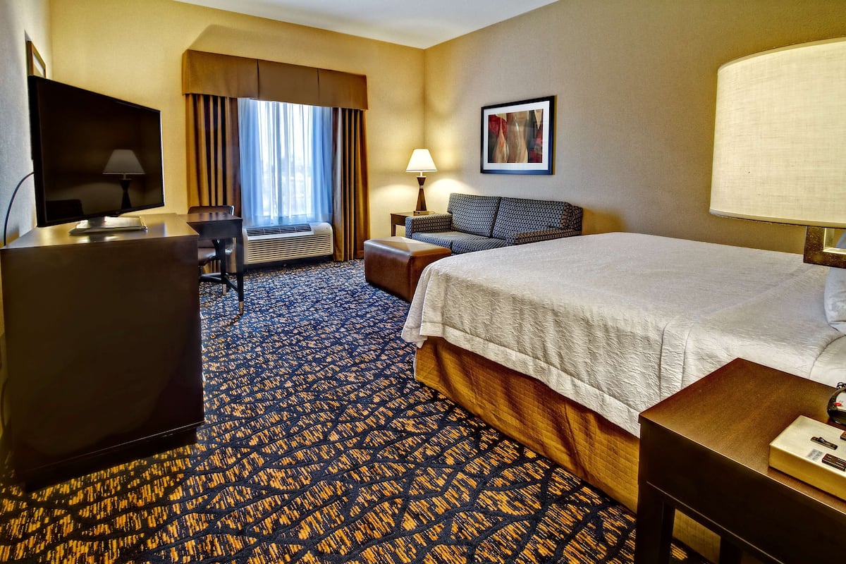 A hotel room with a bed, a desk, a TV, a lamp, and a window with curtains.