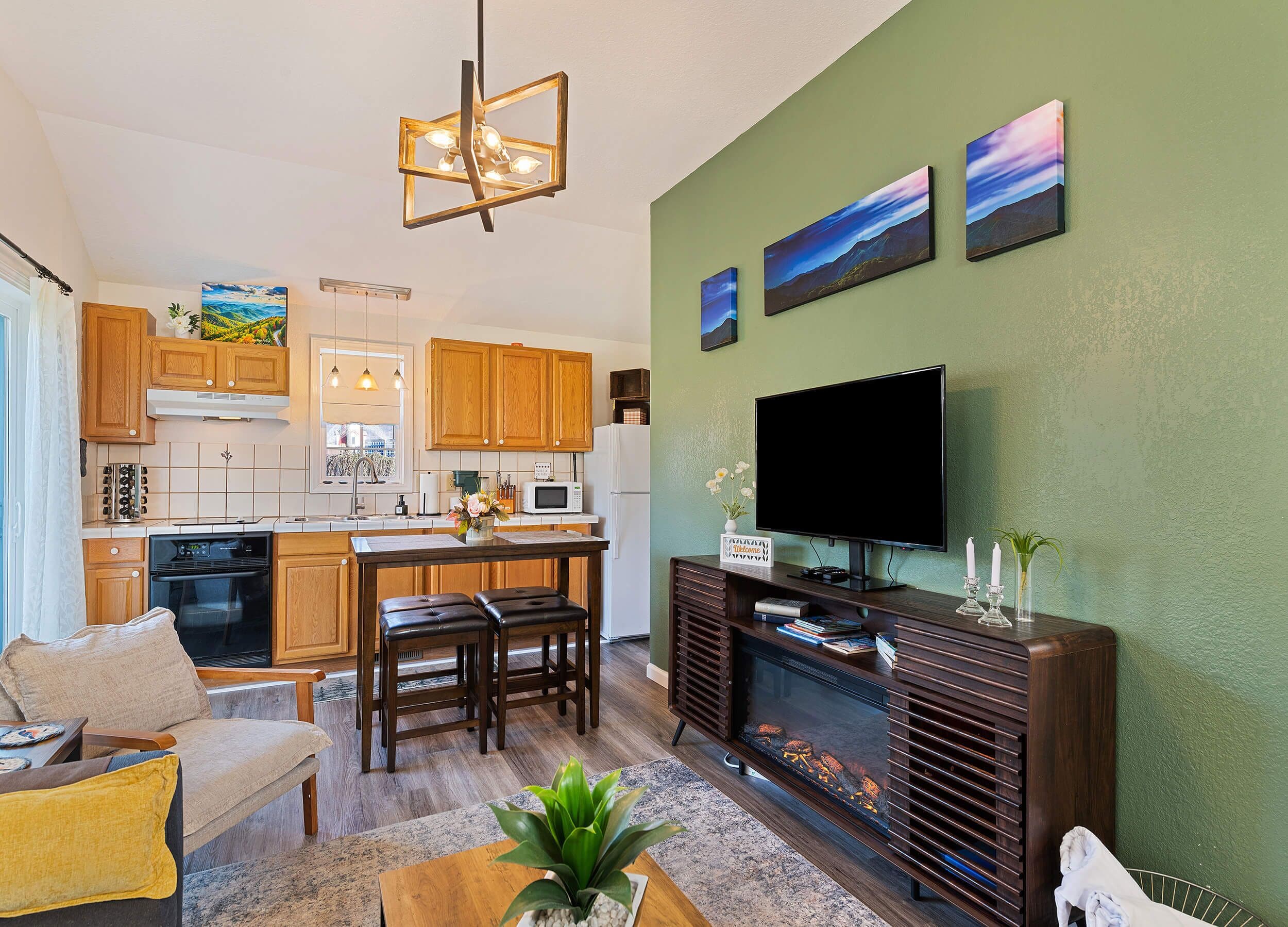 A modern kitchen with wooden cabinets, a dining area with a table and chairs, a flat-screen TV mounted on a wall, and a fireplace.