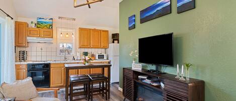 A modern kitchen with wooden cabinets, a dining area with a table and chairs, a flat-screen TV mounted on a wall, and a fireplace.
