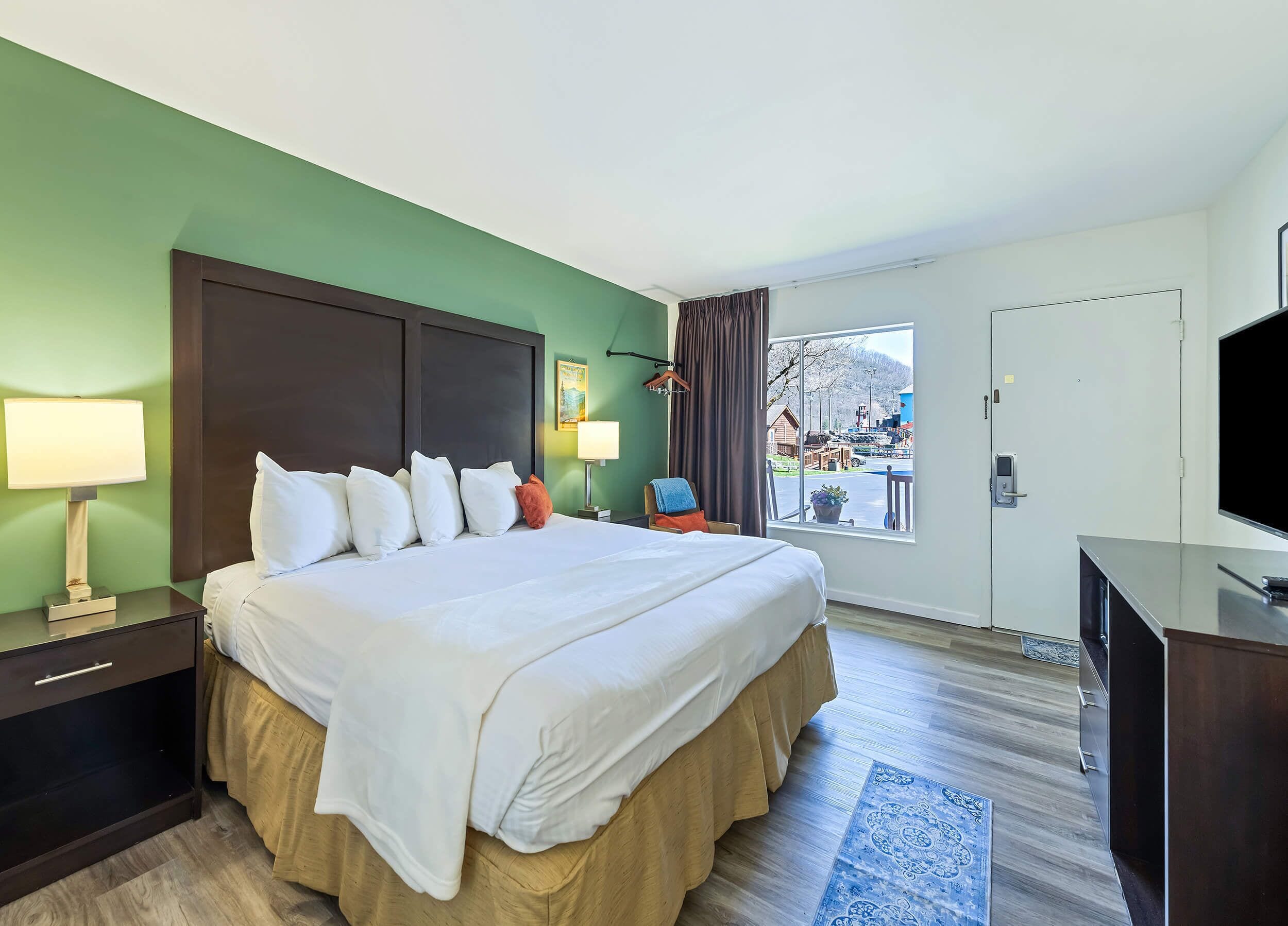 Quarto de hotel com cama, abajures, televisão, janela com vista e porta.