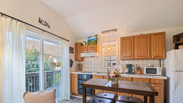 A kitchen with wooden cabinets, a dining table with stools, a microwave, and a refrigerator. - Castlewood Inn (Maggie Valley)