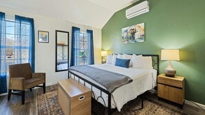 A bedroom with a bed, bedside tables, a chair, a bench, and a window with curtains. - Castlewood Inn (Maggie Valley)