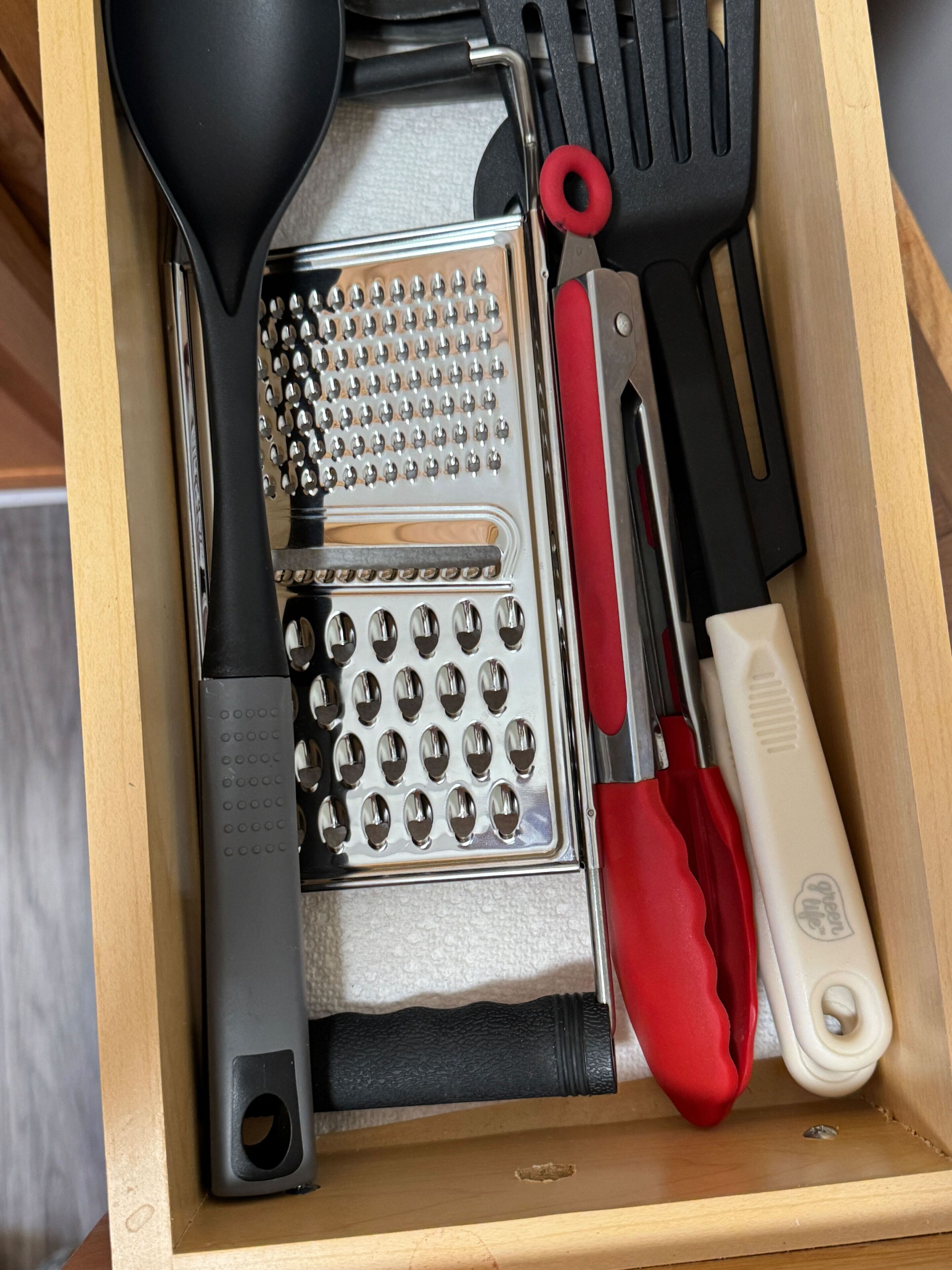 A drawer containing a grater, a spatula, a knife, and a red-handled utensil.