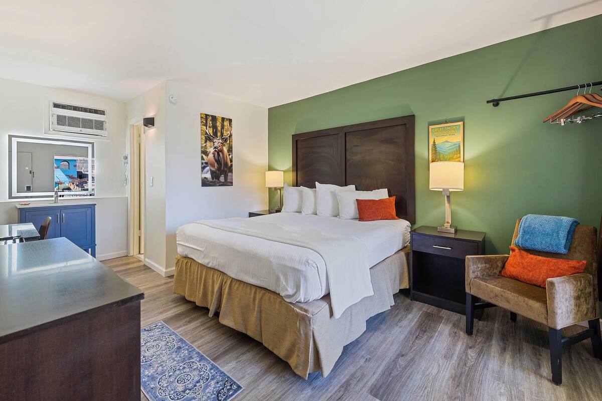 A hotel room with a bed, bedside tables, a desk, a chair, and a mirror.