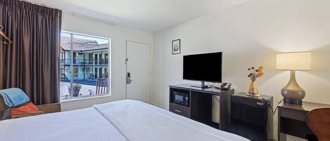 A hotel room with a bed, a desk with a computer, a TV, a lamp, and a view of the street.