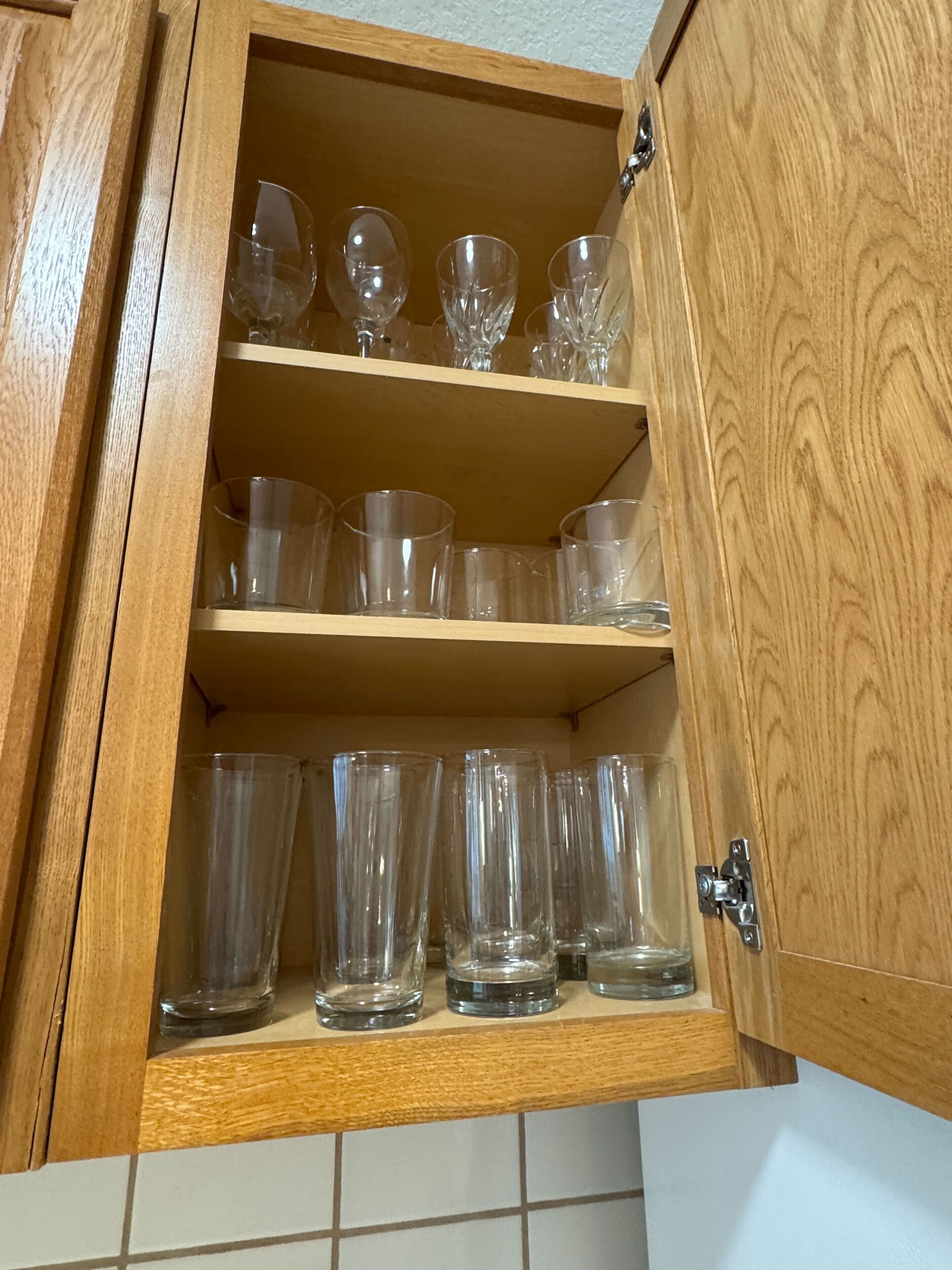 A wooden cabinet with multiple shelves containing clear glassware.