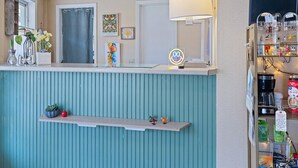 A reception area with a counter, a wall-mounted lamp, framed artwork, a neon sign, and a shelf with small items. - Castlewood Inn (Maggie Valley)
